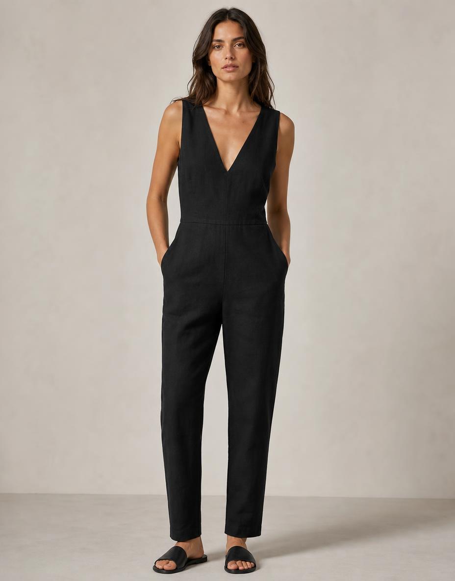 NotchGrain demo photograph — One-piece sleeveless jumpsuit in black linen: deep V-neckline, no sleeves, a visible horizontal waist seam joining bodice to trouser, and narrow straight legs of constant width to an ankle-length hem.